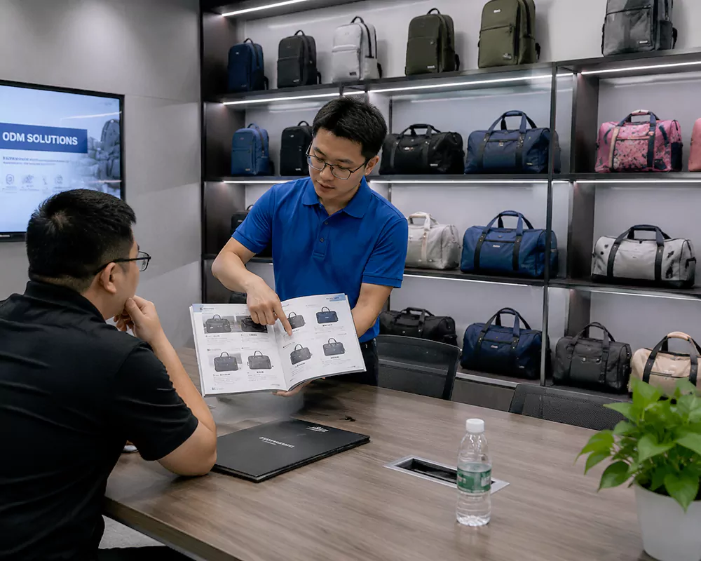Factory representative showing a catalog of pre-designed bags to a B2B buyer in a showroom.